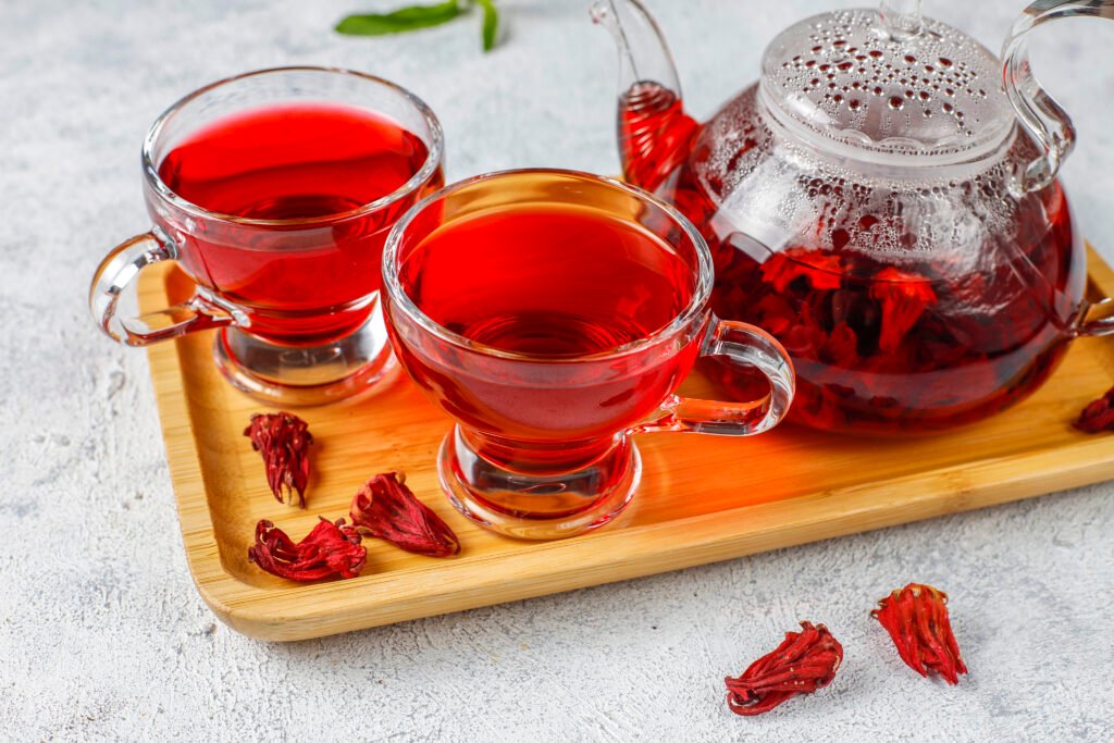 A steaming cup of Friska Tea with herbal ingredients surrounding it—Moringa, Graviola, Hibiscus, and Fenugreek